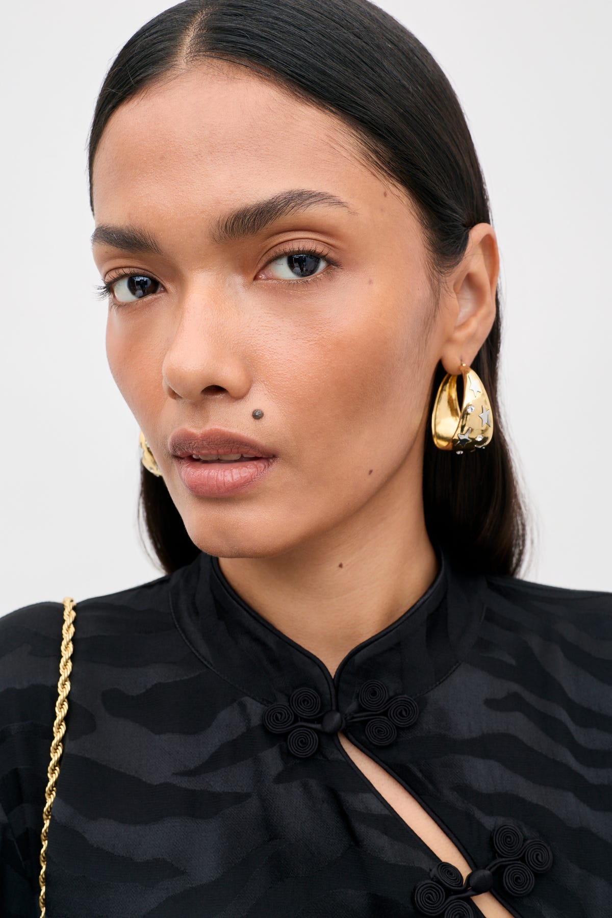 Close-up of a person wearing Sergio - Gold chunky, gold-toned hoop earrings with inlaid silver star accents.