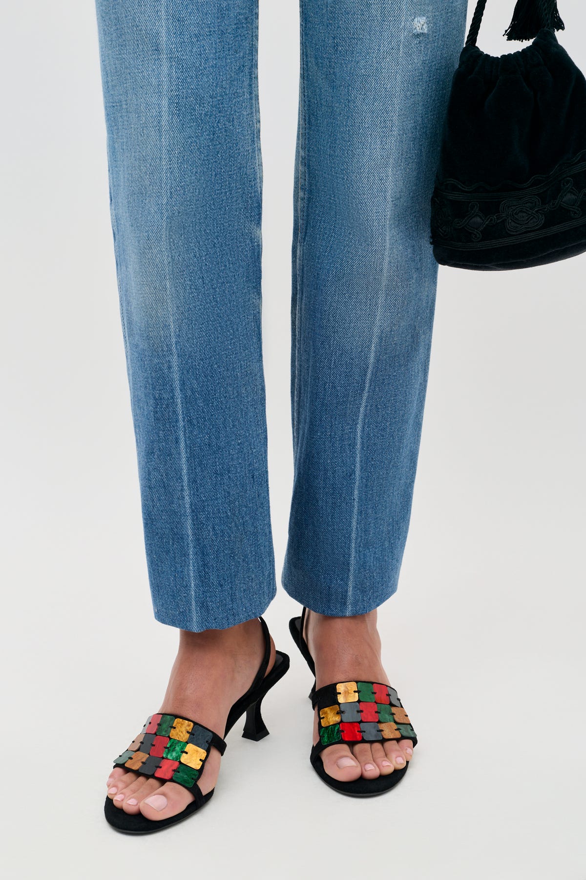 Indie - Multi black slingback sandals featuring a strap of colorful, jigsaw-shaped embellishments, worn with blue jeans and a black handbag.