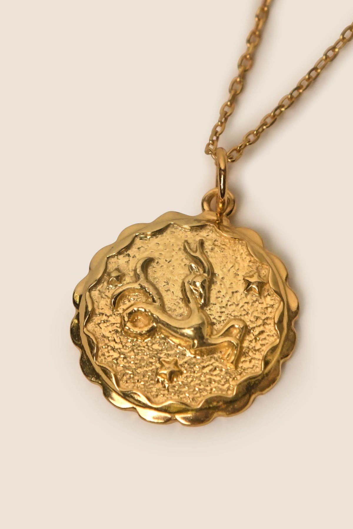 Zodiac - Capricorn: A gold vermeil necklace with a round, scalloped-edge charm featuring an embossed Capricorn symbol and tiny stars on a textured background—a celestial piece for your jewelry collection.