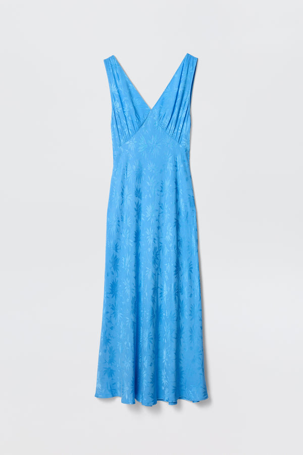 The Sandrine - Daisy Jacquard Blue by RIXO is a sleeveless, light blue V-neck midi slip dress with a subtle daisy jacquard pattern, shown on a plain white background.