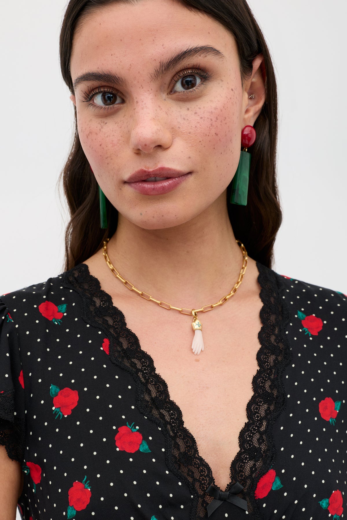 A woman with long brown hair, natural makeup, and vintage-inspired jewellery wears the Adara - Gold earrings and a black dress with red rose and white polka dots, looking at the camera against a plain background.