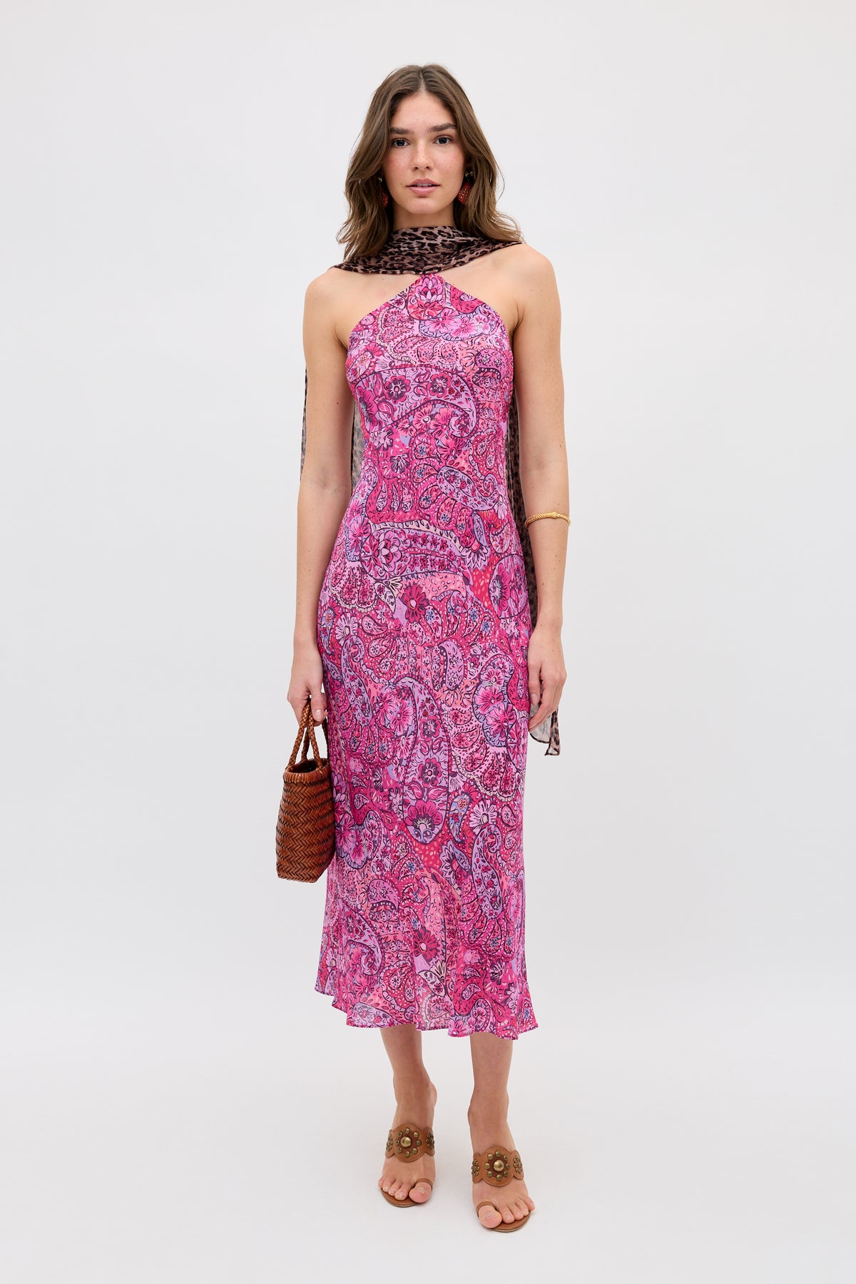 A woman faces forward wearing the Hayley - Leopard Paisley Mix Multi sleeveless midi dress, paired with a brown woven handbag, brown sandals, and a dark patterned scarf, set against a plain white background.