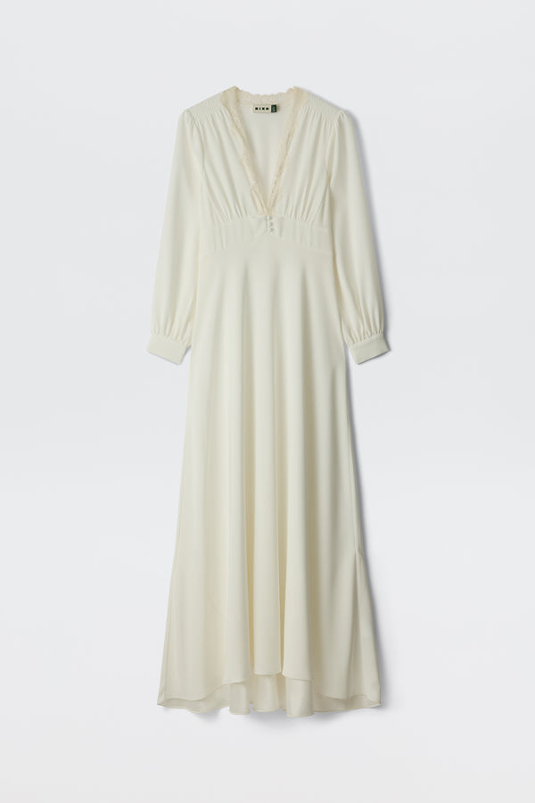 The Emory - Ivory Lace is a long, flowing ivory lace gown with long sleeves, a V-neckline, delicate lace trim, and satin back crepe bodice with button details, displayed against a white background.