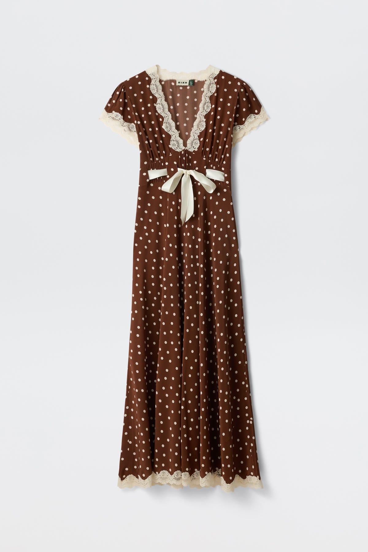 Marlice - Layla Dot Brown is a brown, floor-length dress featuring white polka dots, cream lace trim on the sleeves, neckline, and hem, a deep V-neckline, short sleeves, and a cream ribbon bow accentuating the waist.