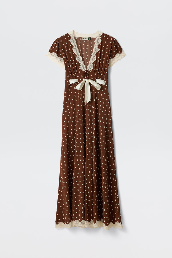 Marlice - Layla Dot Brown is a brown, floor-length dress featuring white polka dots, cream lace trim on the sleeves, neckline, and hem, a deep V-neckline, short sleeves, and a cream ribbon bow accentuating the waist.