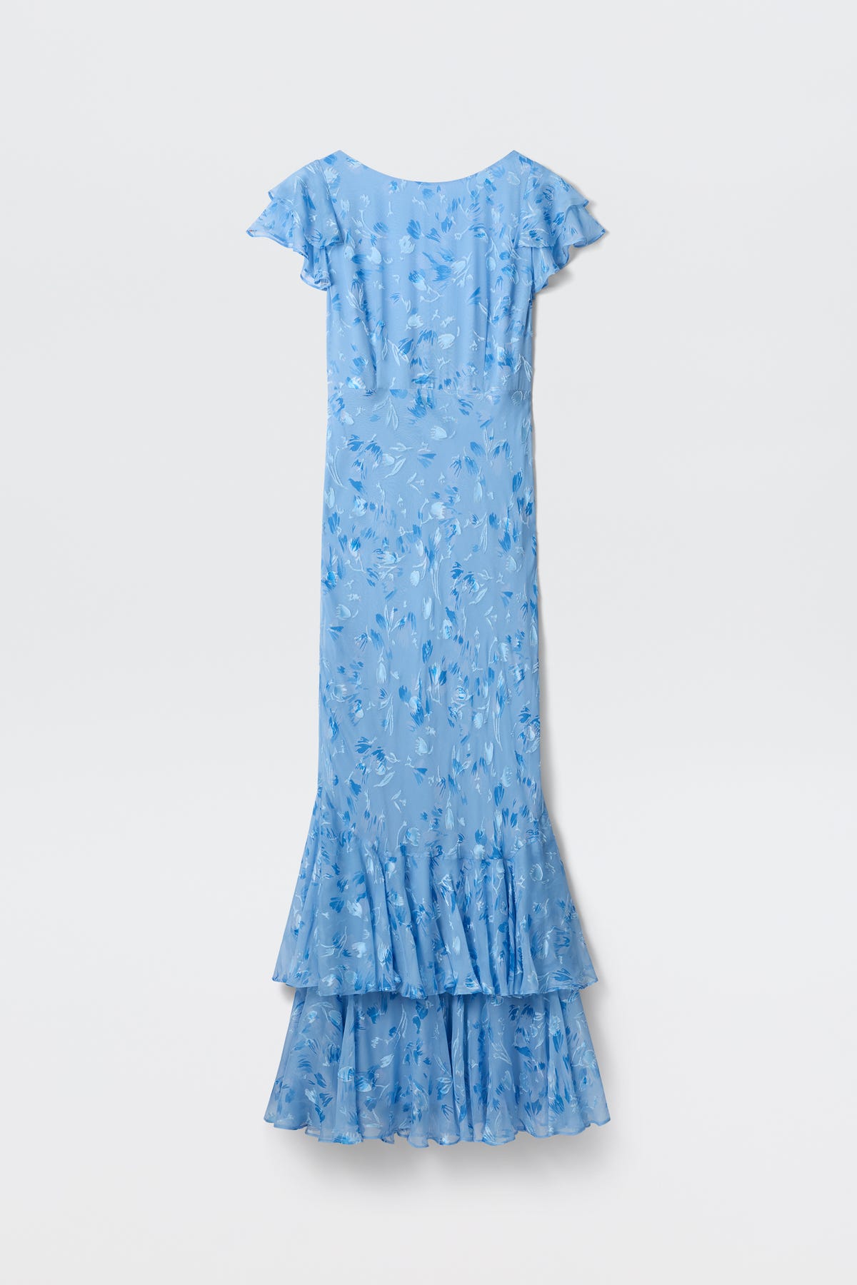 The Ordinia - Ava Devore Blue is a long, light blue dress with a floral pattern, short flutter sleeves, and a layered ruffled hem, shown against a plain white background.