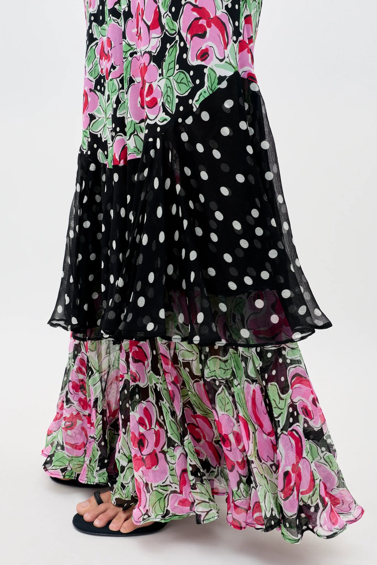 Wearing the Ordinia - Rose Dot Mix Black, a long flowy skirt featuring pink and green floral patterns with black and white polka dots, paired with simple black sandals. The background is plain white.
