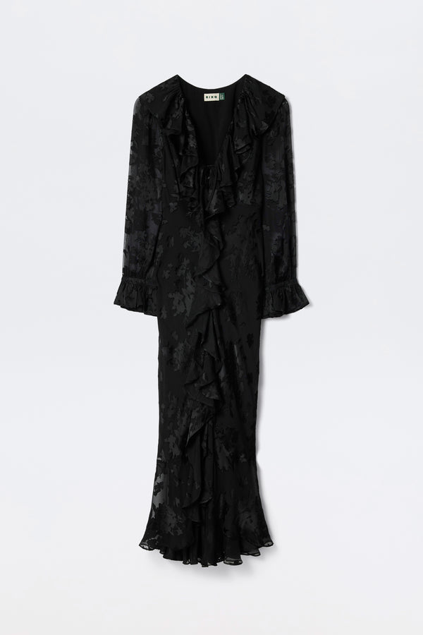 The Gracye - Bouquet Devoré Black is a long-sleeved, ankle-length black dress featuring a subtle floral pattern, ruffled V-neckline, ruffled cuffs, and a ruffled hem, shown against a plain white background.