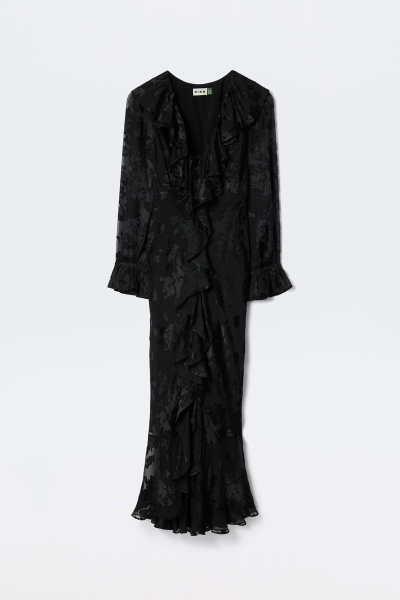 The Gracye - Bouquet Devoré Black is a long-sleeved, ankle-length black dress featuring a subtle floral pattern, ruffled V-neckline, ruffled cuffs, and a ruffled hem, shown against a plain white background.