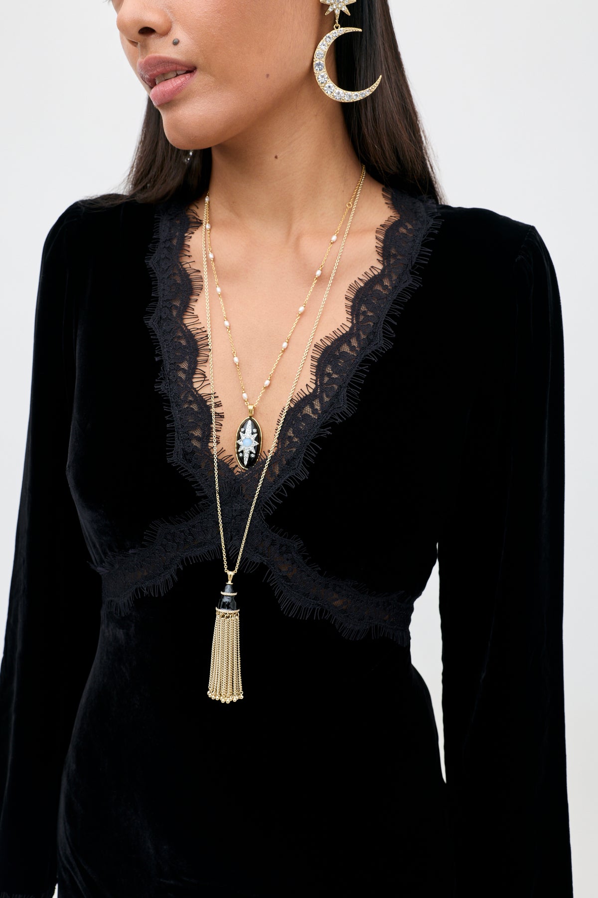 A model in the Alessi - Black velvet dress wears two gold necklaces with star and tassel pendants, paired with large gold moon and star drop earrings for a look of boho-glamour.