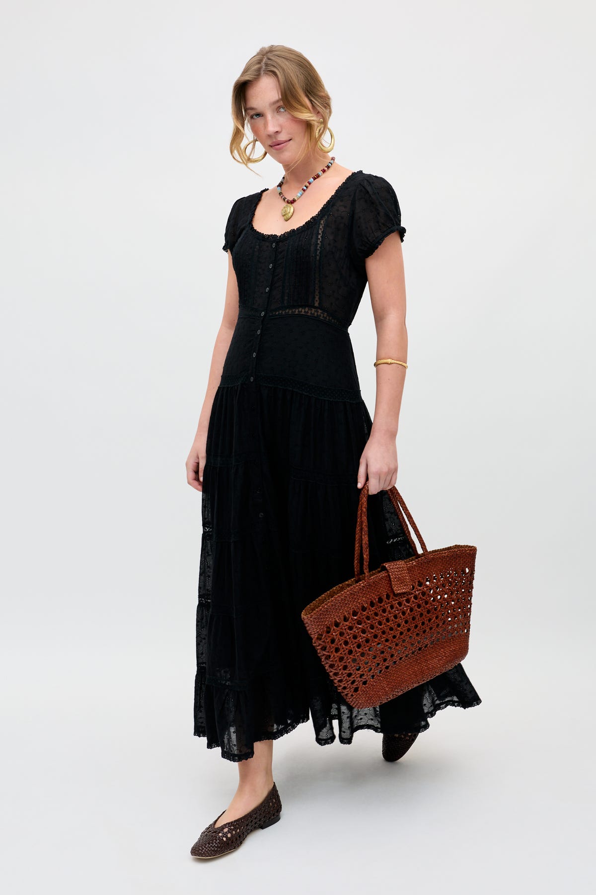 A woman wears the Parma - Multi, a black short-sleeve button-down midi dress, styled with a brown woven handbag, matching flats, necklace, and bracelet, standing against a plain light background.