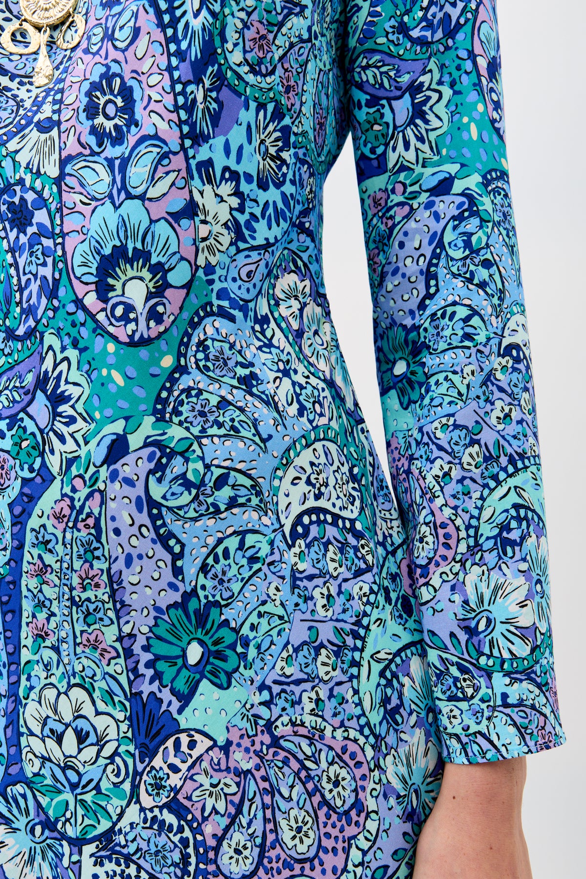 A close-up of a person wearing the Dulce - Paisley Floral Blue, a long-sleeved garment featuring a vibrant blue, teal, and purple floral paisley pattern. Only the torso and arm are visible.