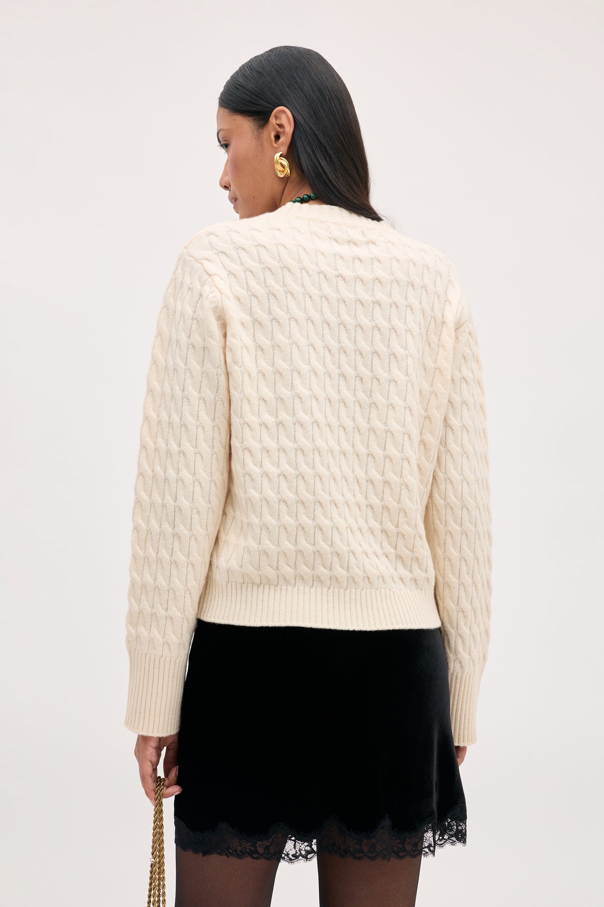A person seen from behind wearing an off-white cable-knit sweater and the Kornelia - Black skirt with a lace trim.