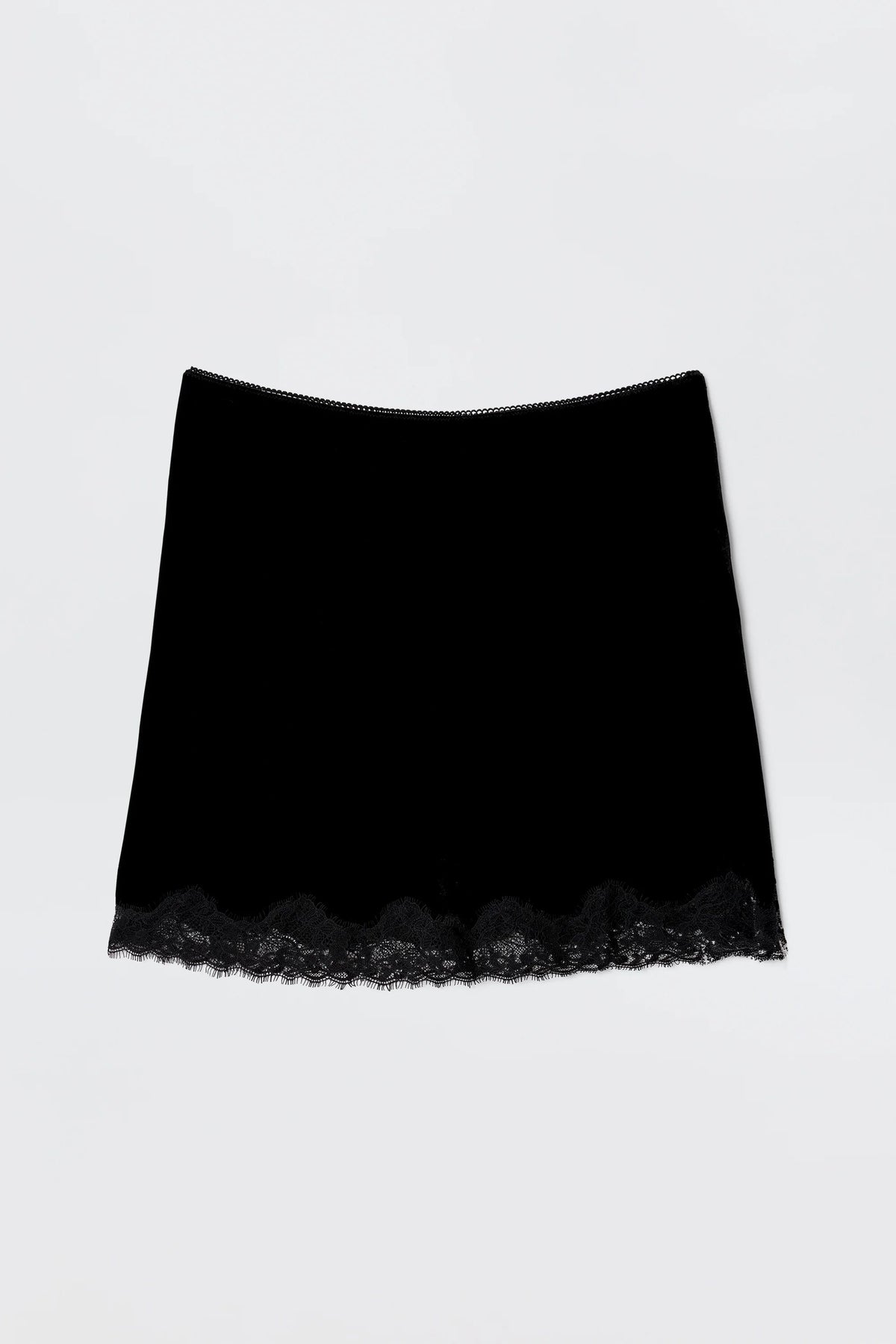 The Kornelia - Black is a nineties-inspired black velvet mini skirt with a straight fit and delicate lace trim at the hem, shown against a plain light background.