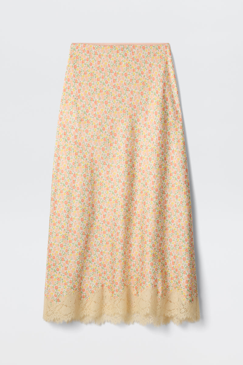 The Matilde - Katie Floral Cream is a long slip skirt in pastel yellow, featuring a colorful floral print and scalloped lace hem, shown on a plain white background.