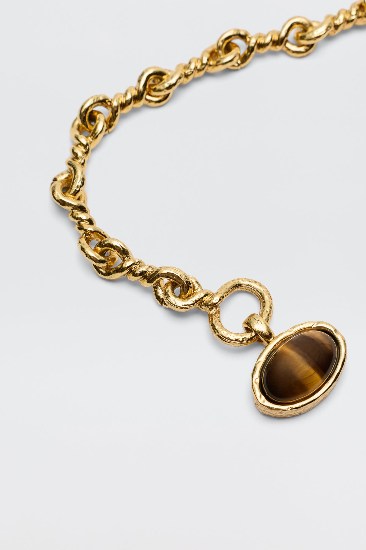 The Zandra - Gold necklace features a chunky, vintage-inspired gold-plated chain with twisted links and a round pendant set with an oval brown gemstone, shown on a light background.
