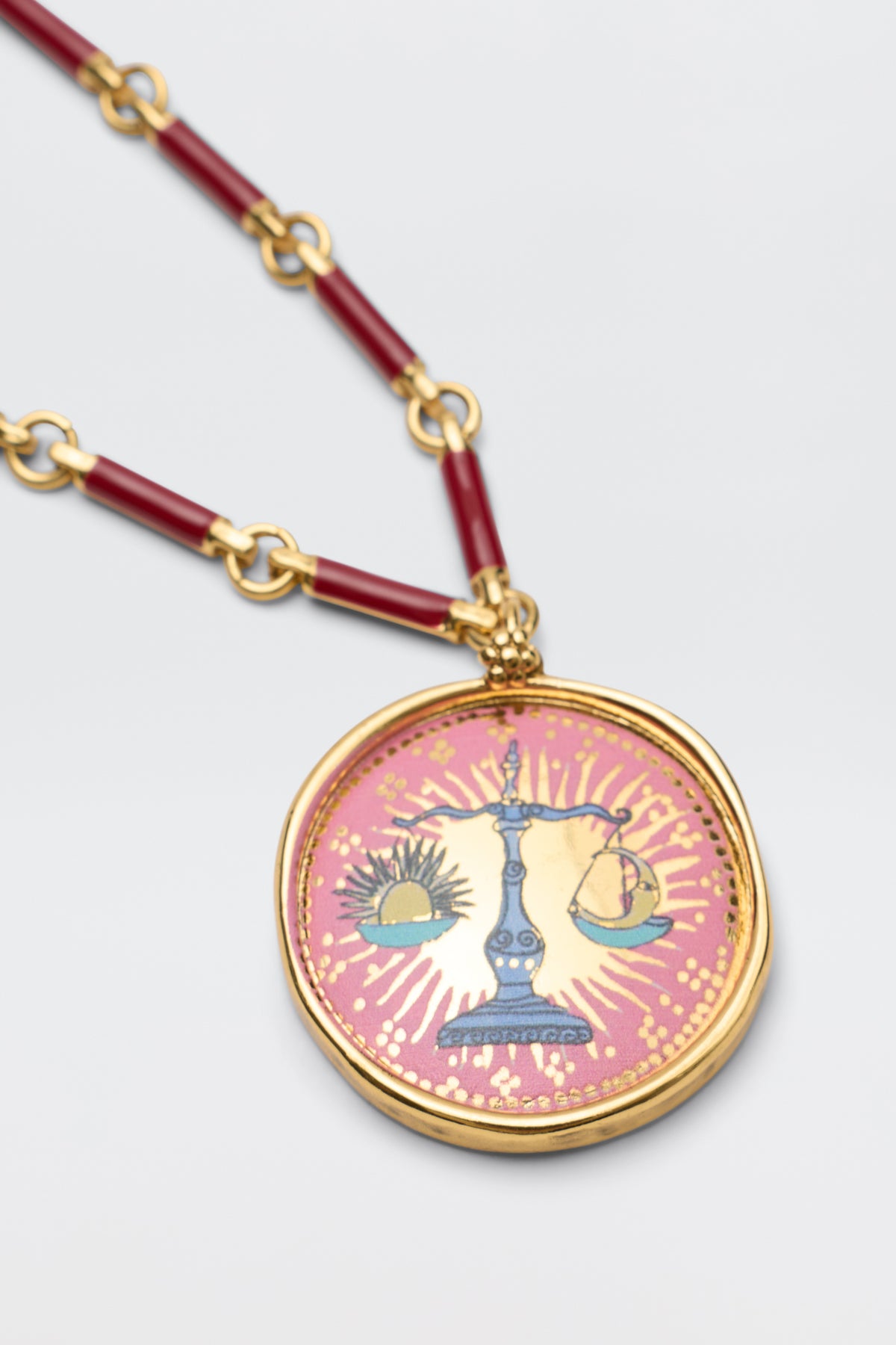 Ari - Astro Libra round gold necklace featuring a scale design with a sun and moon on a pink background, suspended from a red and gold link chain.