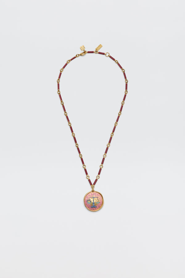 Ari - Astro Libra gold necklace on a link chain featuring maroon beads and a round pendant with a scale icon against a pink sunburst background.