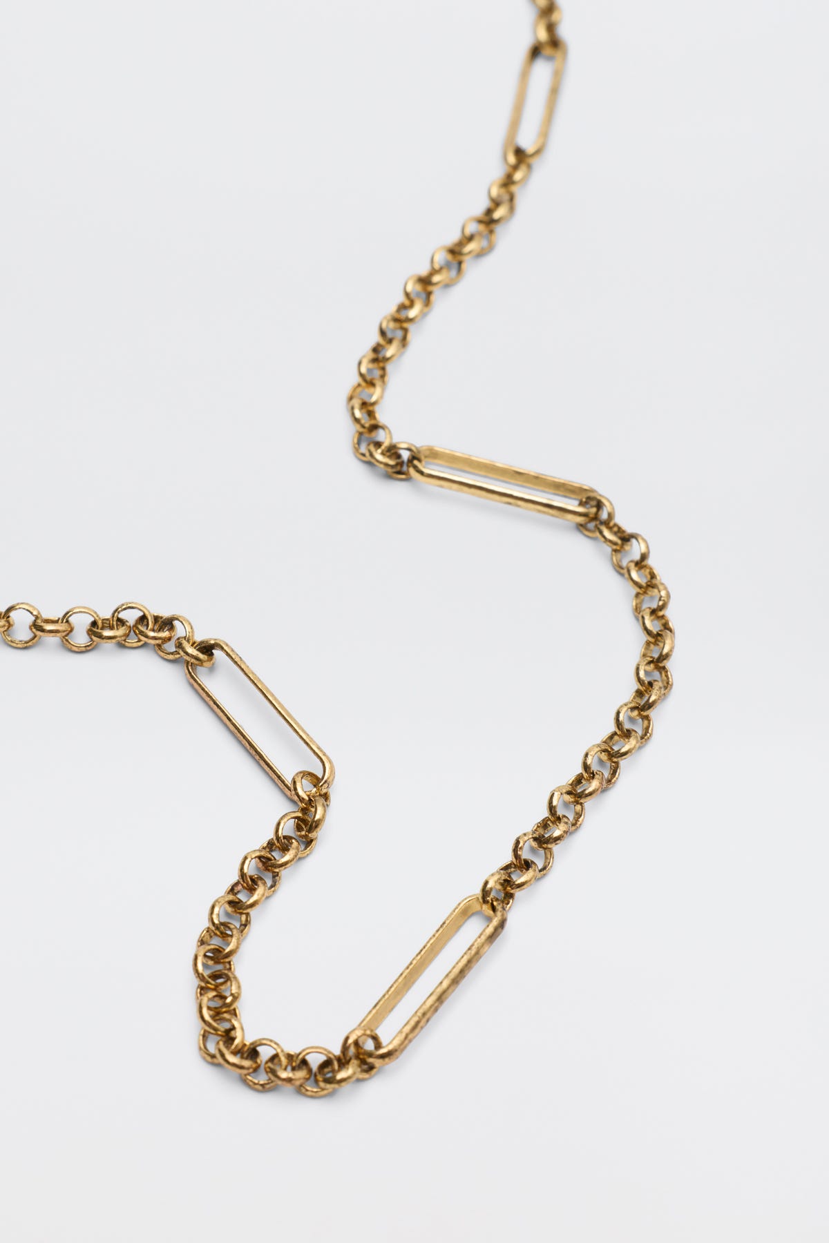 The Eta Gold necklace features alternating small round and elongated oval links, showcased on a plain white background.