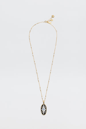Introducing the Andi - Black necklace: a delicate gold chain adorned with small beads and an oval pendant, featuring a clear marquise-cut gemstone set in a striking black and gold frame, beautifully displayed on a white background.
