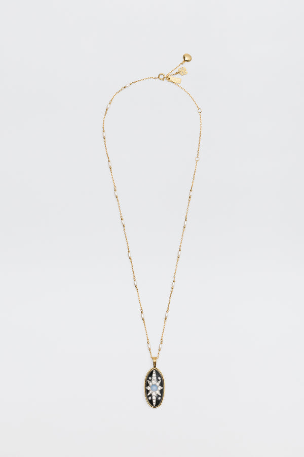 Introducing the Andi - Black necklace: a delicate gold chain adorned with small beads and an oval pendant, featuring a clear marquise-cut gemstone set in a striking black and gold frame, beautifully displayed on a white background.