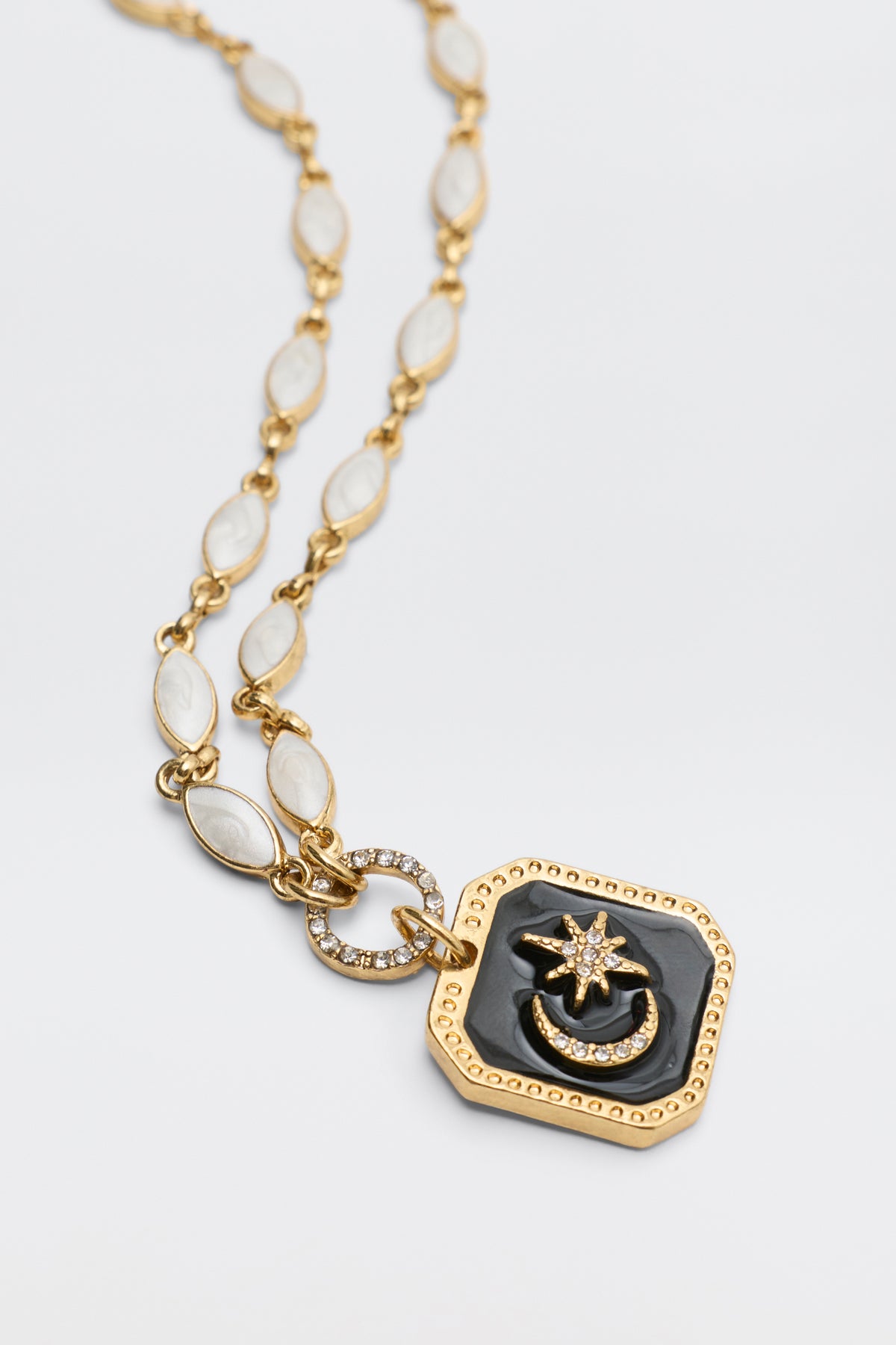 Kathryn - Pearl: A gold necklace featuring oval, pearl-inspired links and a square pendant with a star and crescent design on black enamel, accented by delicate sparkling stones.