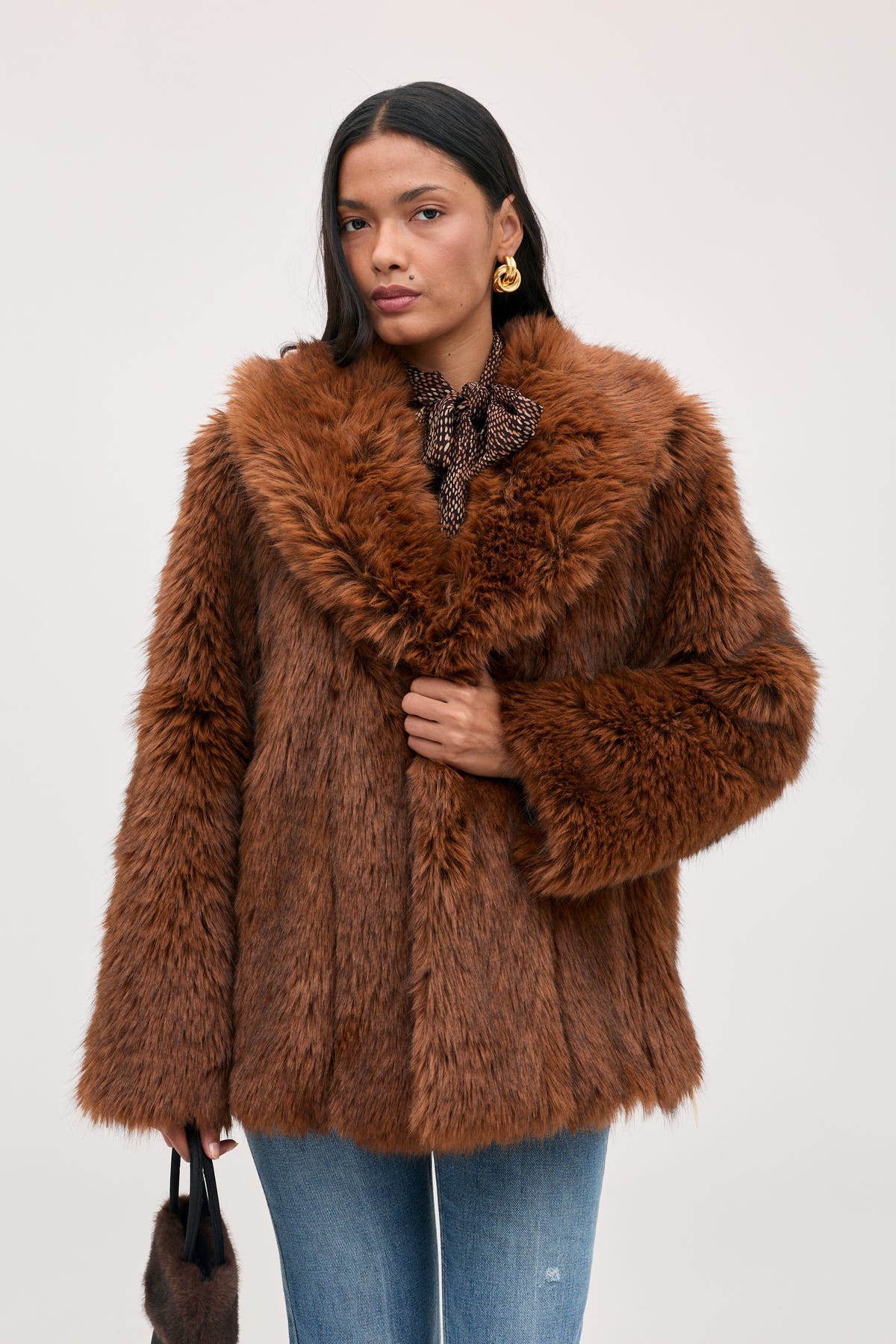 A person wearing a Cybil - Brown faux fur coat with a wide collar and jeans.