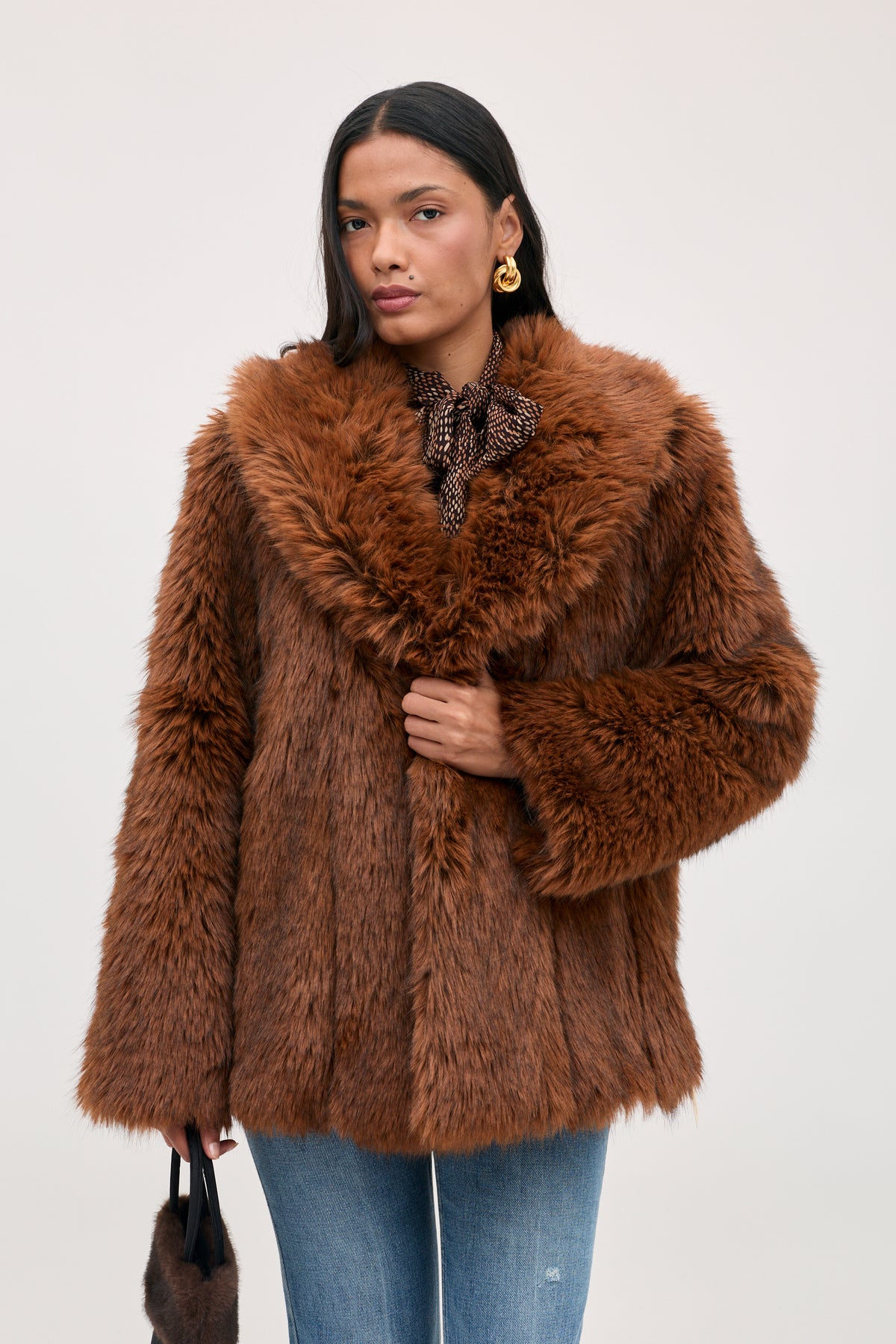 A person wearing a Cybil - Brown faux fur coat with a wide collar and jeans.