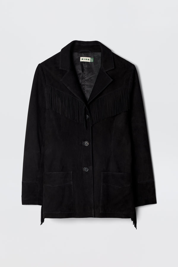 The Teagan - Black is a suede blazer-style jacket with fringe across the chest and back, front button closure, notched lapels, and two large pockets, shown on a plain light background.