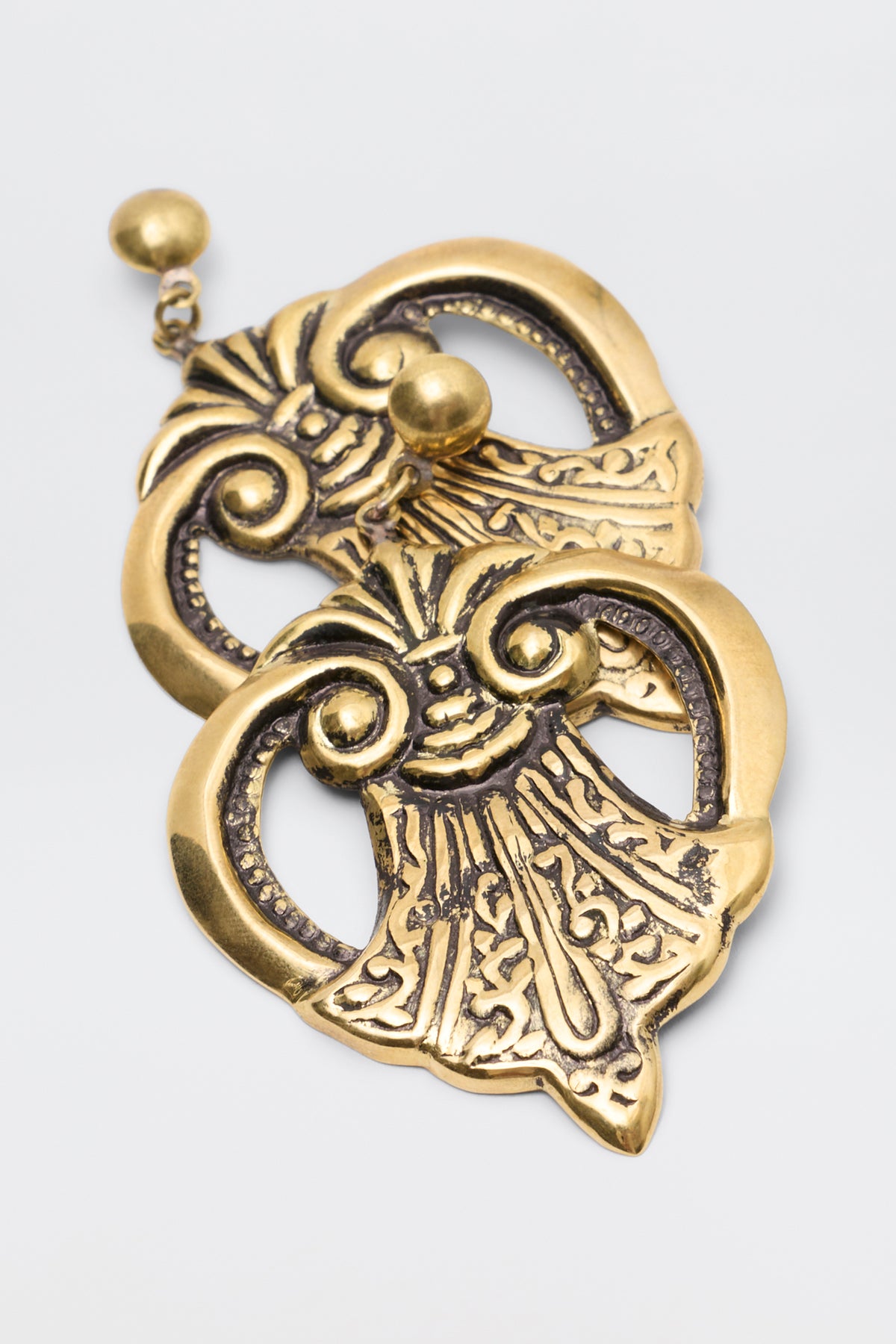 Julieta Earrings Gold: a pair of gold-toned dangle earrings featuring ornate, fan-shaped metal charms with swirling, carved details.