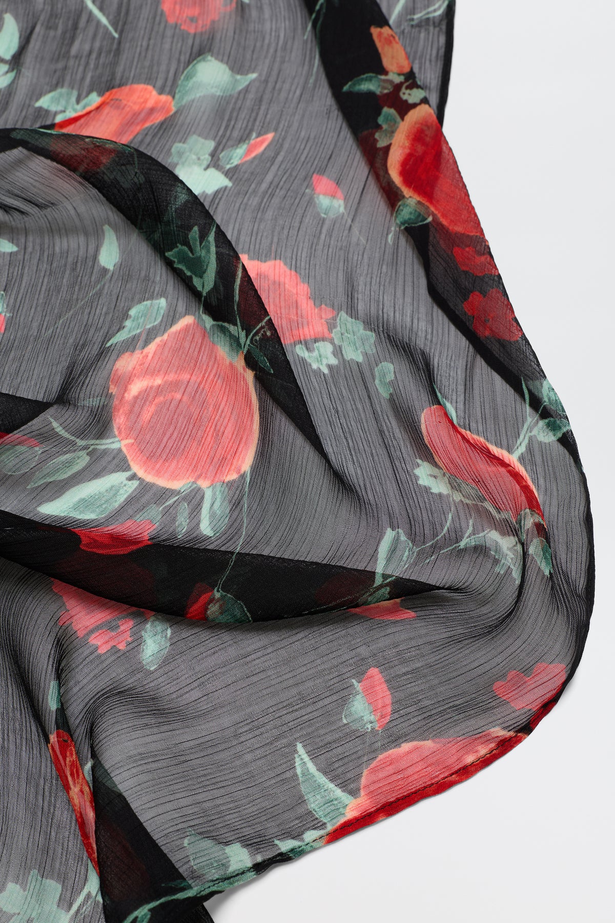 A close-up of the Julien - Claudia Rose Black vintage scarf, featuring sheer black fabric with a floral pattern of red and coral flowers and green leaves, displayed in gentle folds to highlight its textured surface.
