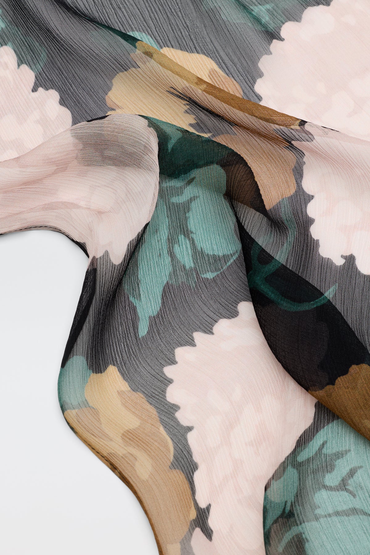 A close-up of Julien - Hydrangea Floral Charcoal sheer fabric, featuring a large hydrangea floral pattern in soft pink, green, beige, and charcoal tones, draped and flowing over a white surface.