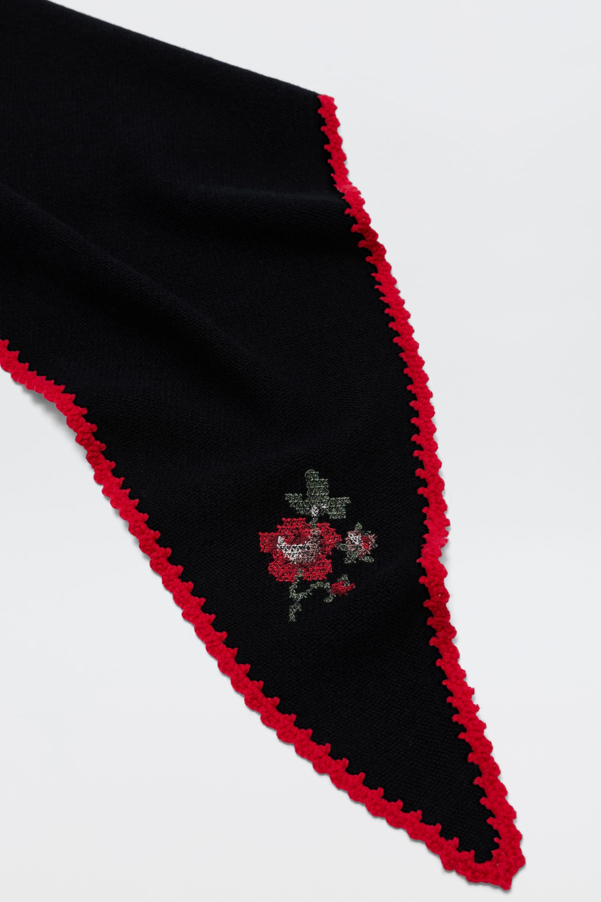 Lianora - Abi Rose Knit Black: A black triangular scarf featuring a red crocheted border and a delicate embroidered red floral motif near the tip, displayed on a white background.