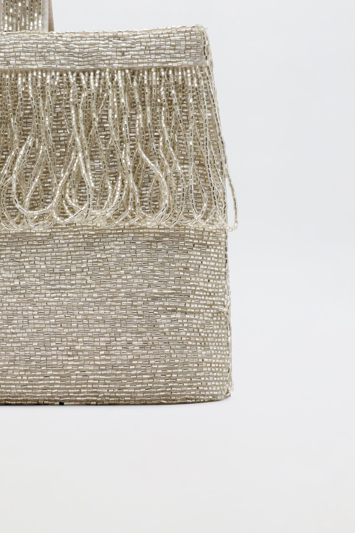 Close-up of Zenni - Beaded Silver rectangular metallic clutch with fringe along the top edge and a rounded top handle, set against a plain light background.