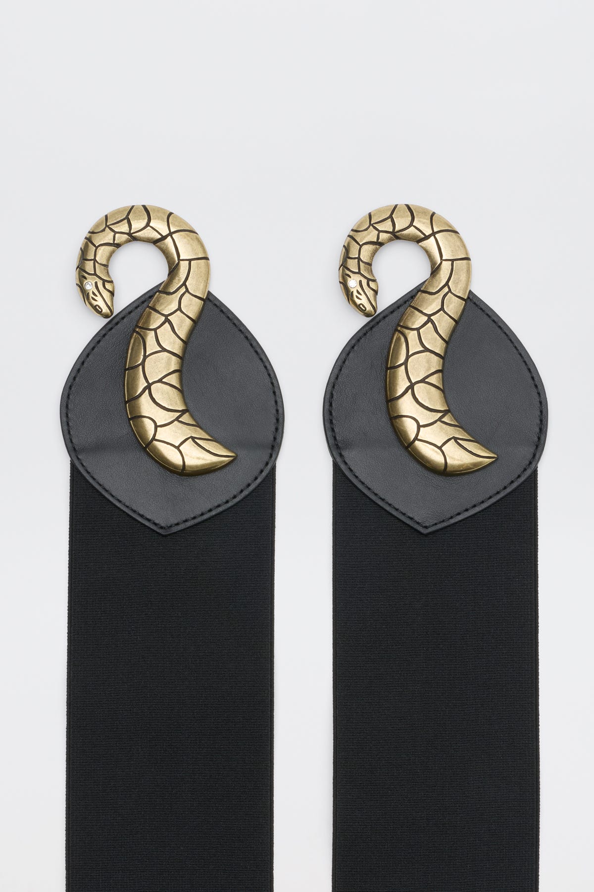Milena - Black features two black elastic straps, each finished with a black leather patch topped by a curved, gold-tone metal snake ornament.