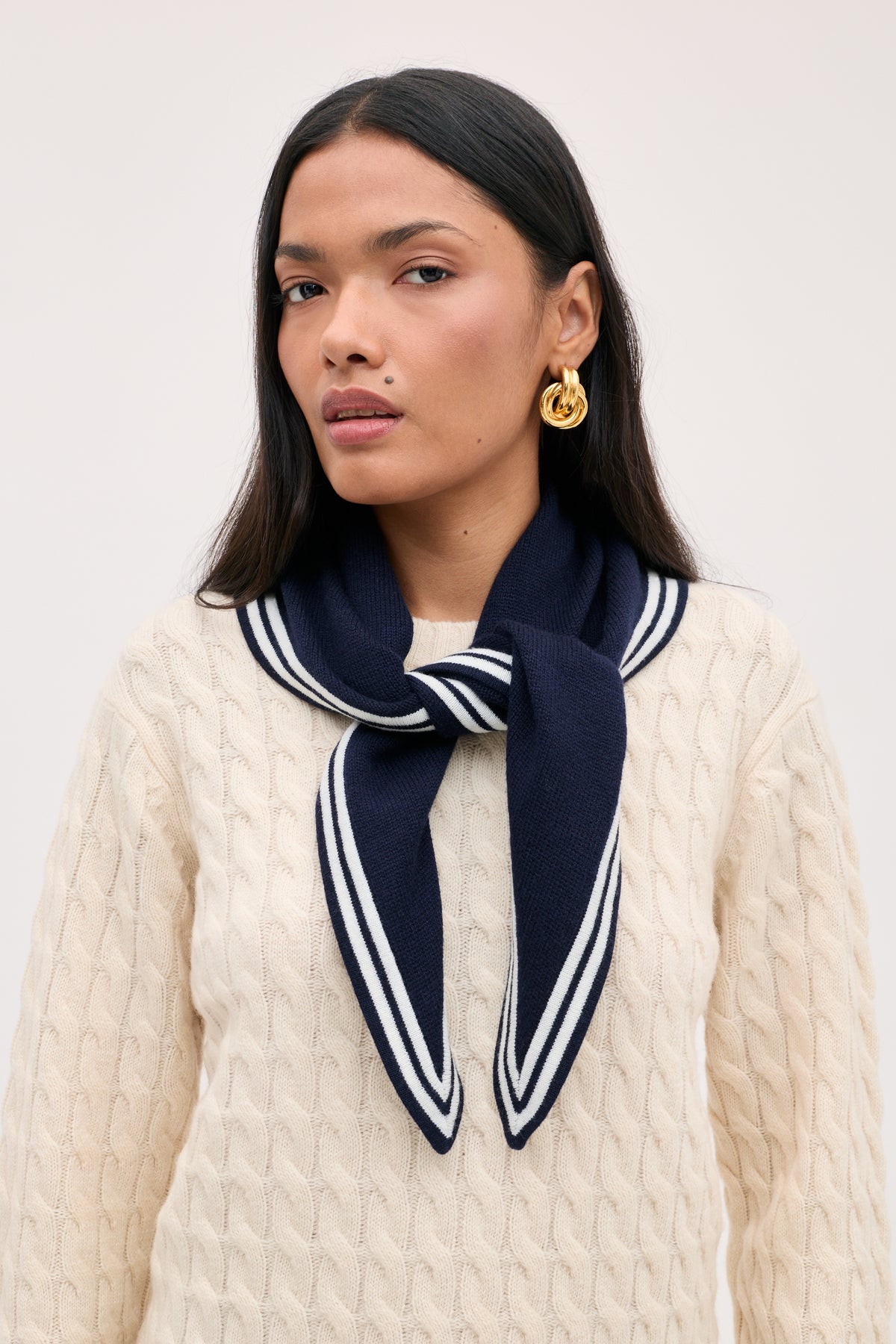 A person wearing a cream cable-knit sweater and a Lianora - Sailor Stripe Navy neck scarf with white stripes.