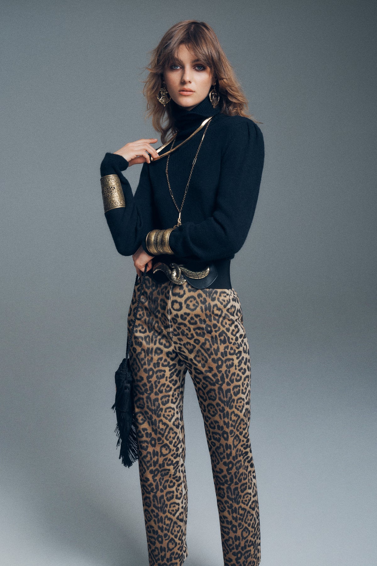 A model wearing a black turtleneck sweater, gold statement jewelry, and Savannah Leopard Brown trousers.