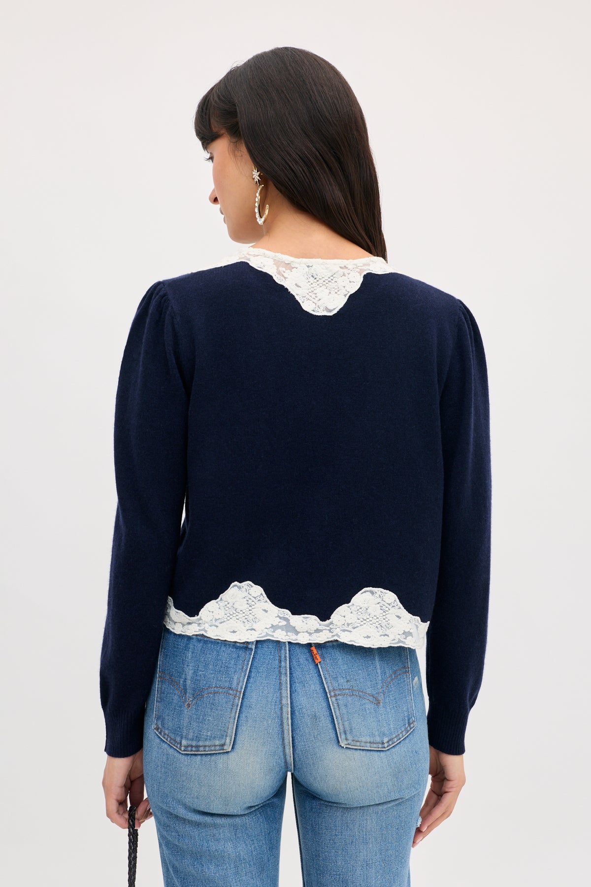 Tassia - Navy long-sleeved sweater in navy blue with white lace trim at the collar and hem, worn with blue jeans.