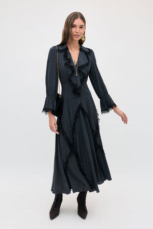 A woman wearing the Aerin - Micro Polka Dot Black midi-length dress with white micro polka dots, black lace trim, and a ruffled neckline, paired with black lace-up ankle boots.