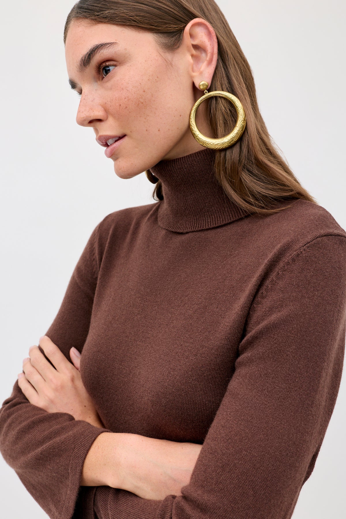 A person wearing the Aly - Chocolate brown turtleneck sweater and large gold hoop earrings.