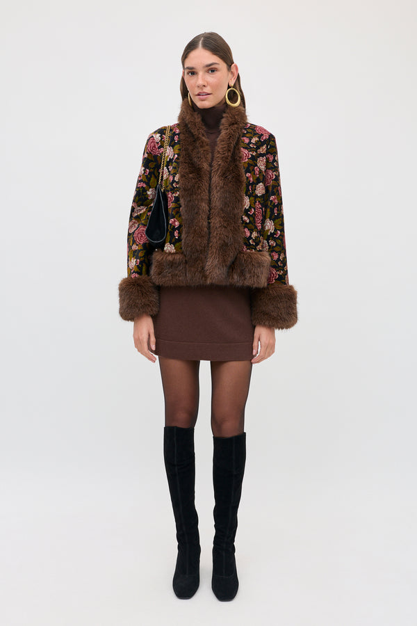 A person wearing an Aly - Chocolate floral print jacket with faux fur trim over a brown dress and black knee-high boots.