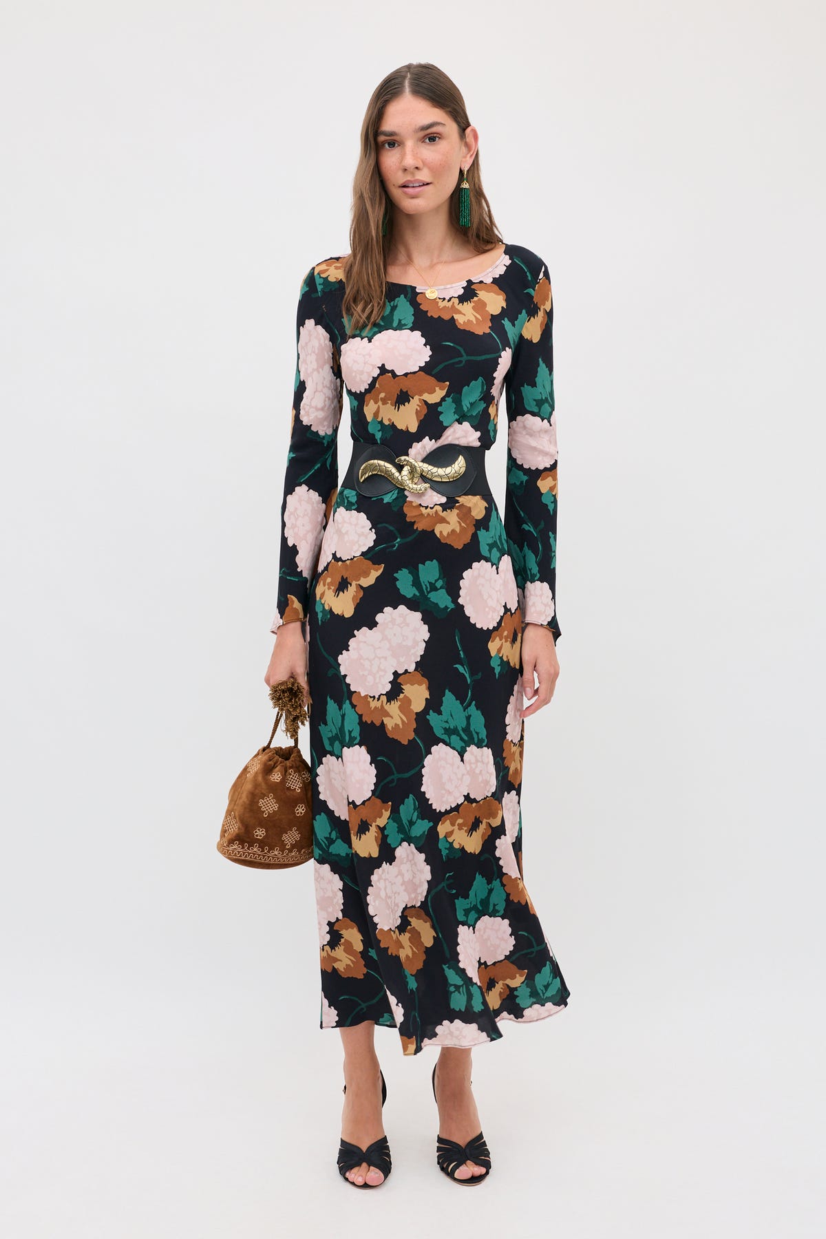 A woman wearing the Amal - Hydrangea Floral Charcoal long-sleeved midi dress, accented by a wide black belt with a gold buckle and holding a small brown pouch.