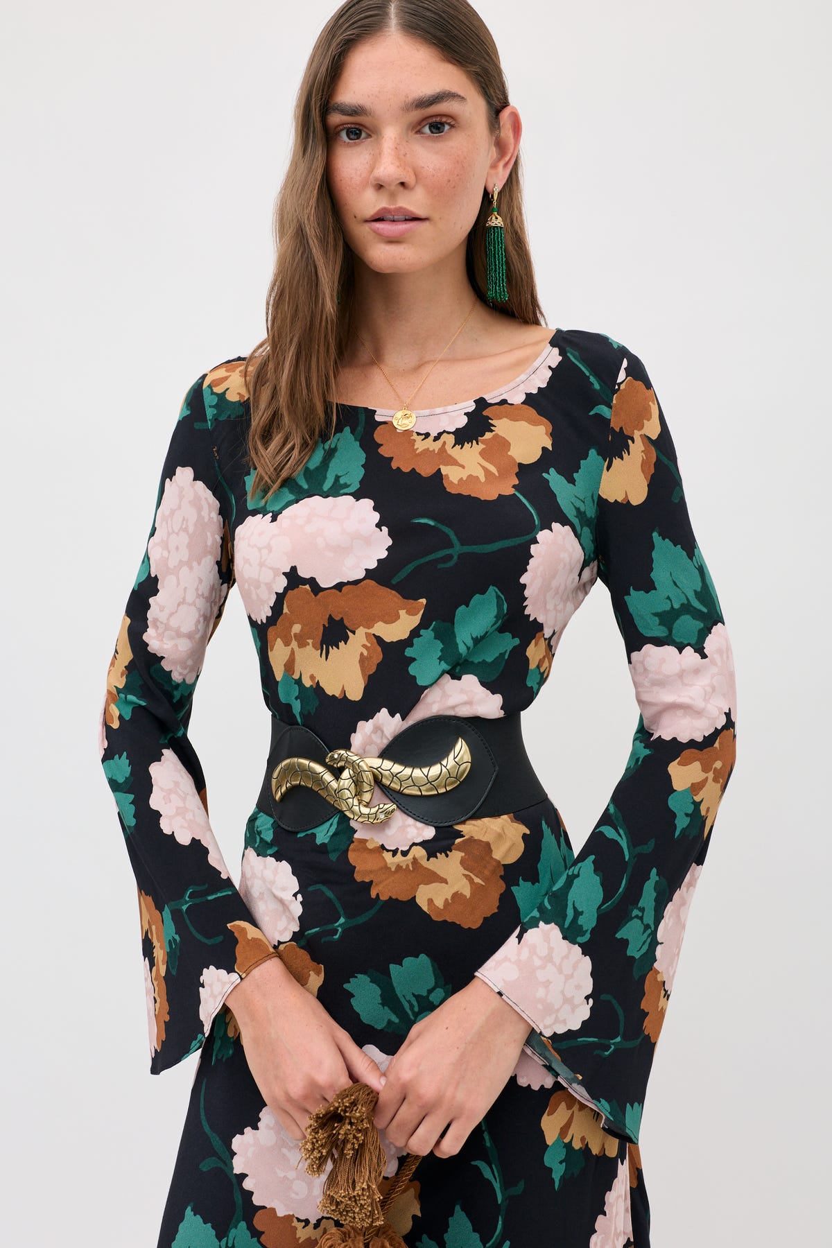 A person wears the Amal - Hydrangea Floral Charcoal long-sleeved dress with a large hydrangea print and a wide black belt featuring a gold snake-shaped buckle.