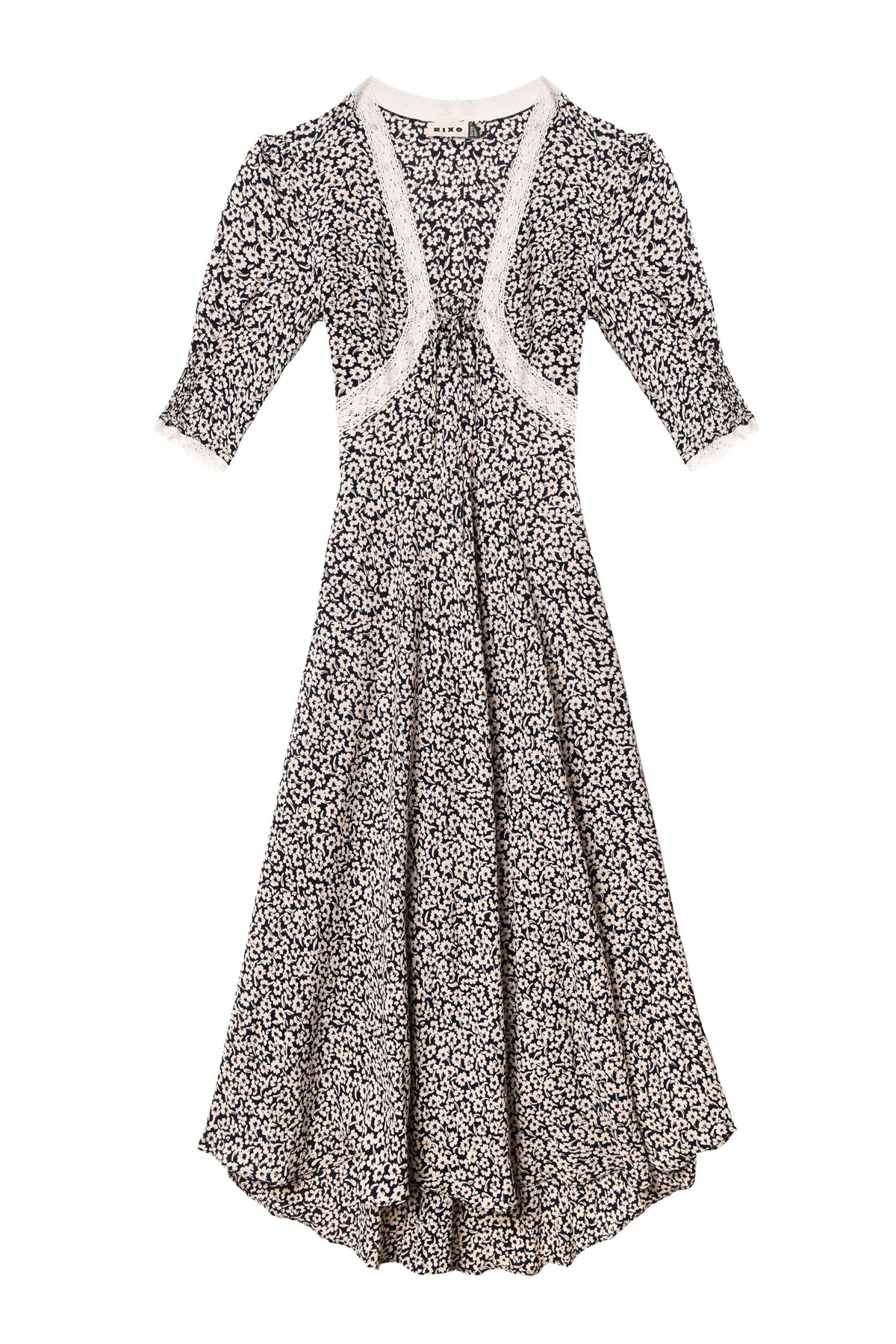 The Amina - English Daisy Deep Navy dress features a vintage-inspired navy blue design with white floral print, lace trim at the neckline and cuffs, short puff sleeves, a fitted waist, and a flared skirt.