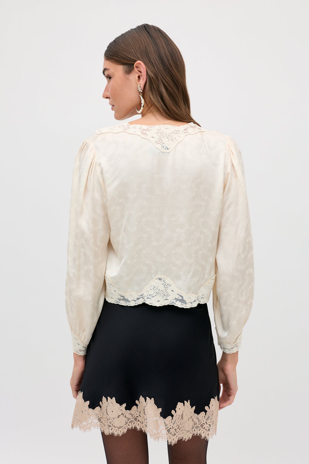 A woman seen from behind wearing an ivory long-sleeved blouse with lace trim and an Ariah - Black skirt with a lace-trimmed hem.