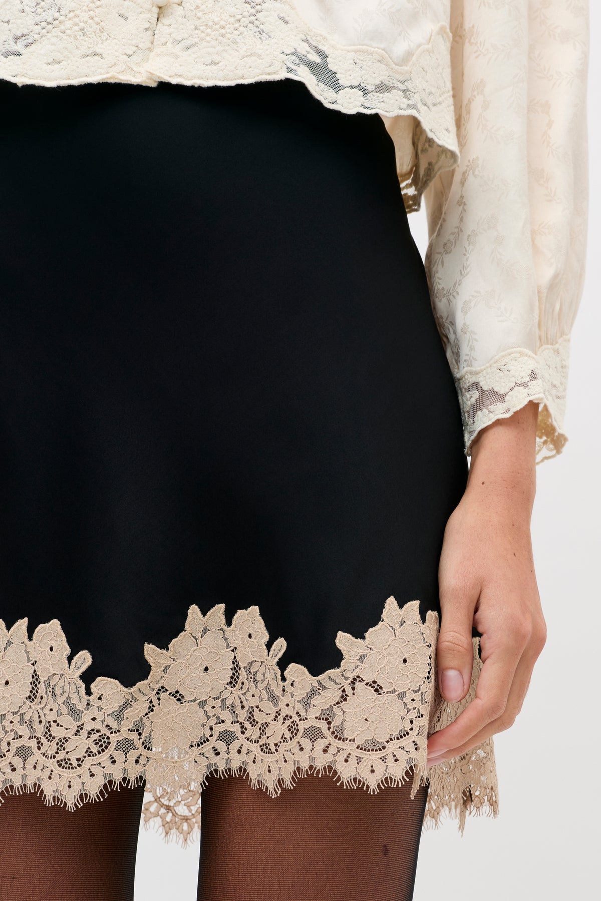 Ariah - Black skirt with a wide, intricate beige lace hem, worn with a cream-colored floral lace blouse.