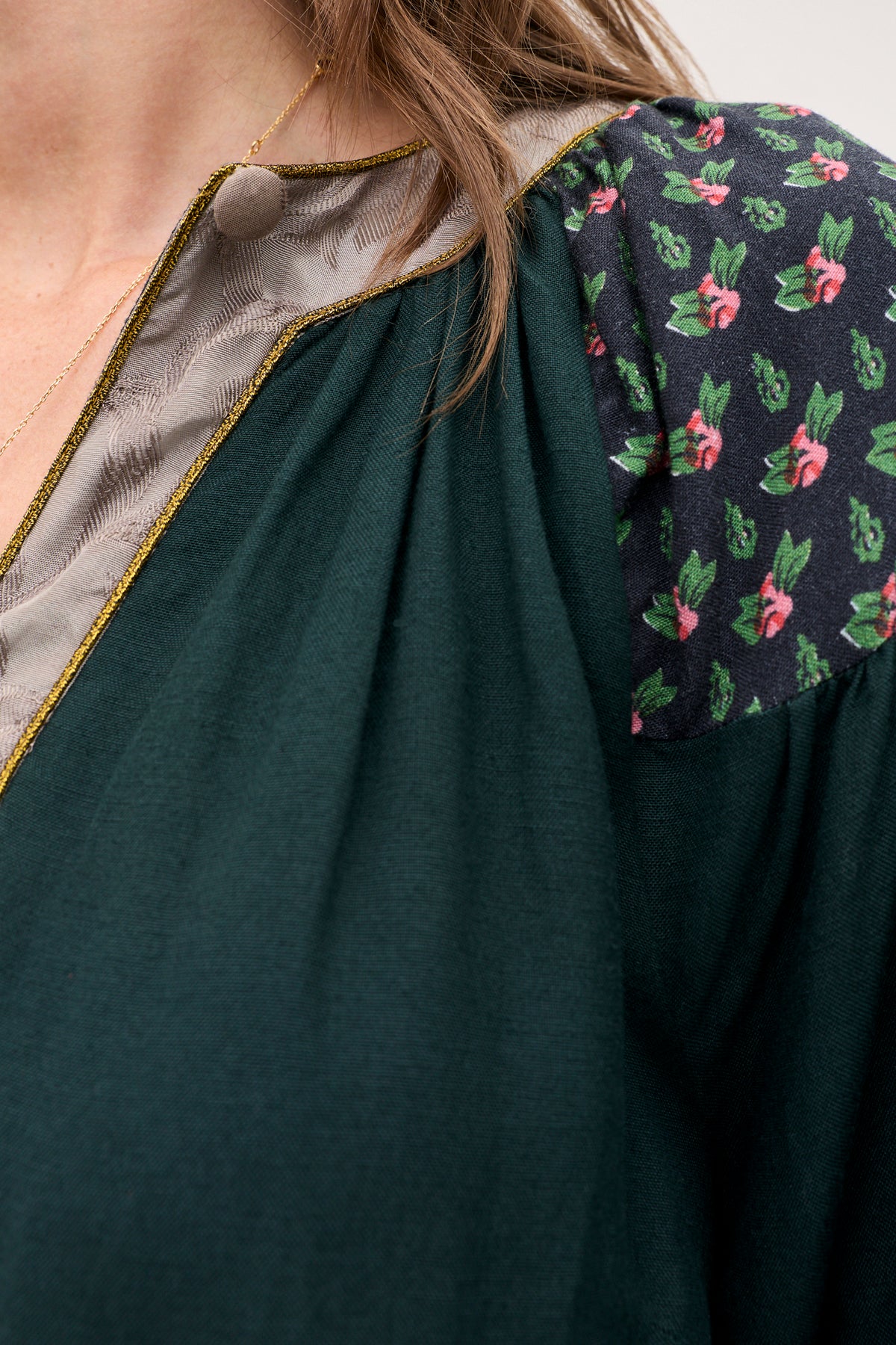 A close-up of the Bria - Rose Mix Pink garment, featuring a dark green design with a gray inner collar, gold trim, and a black shoulder panel patterned with small pink flowers.