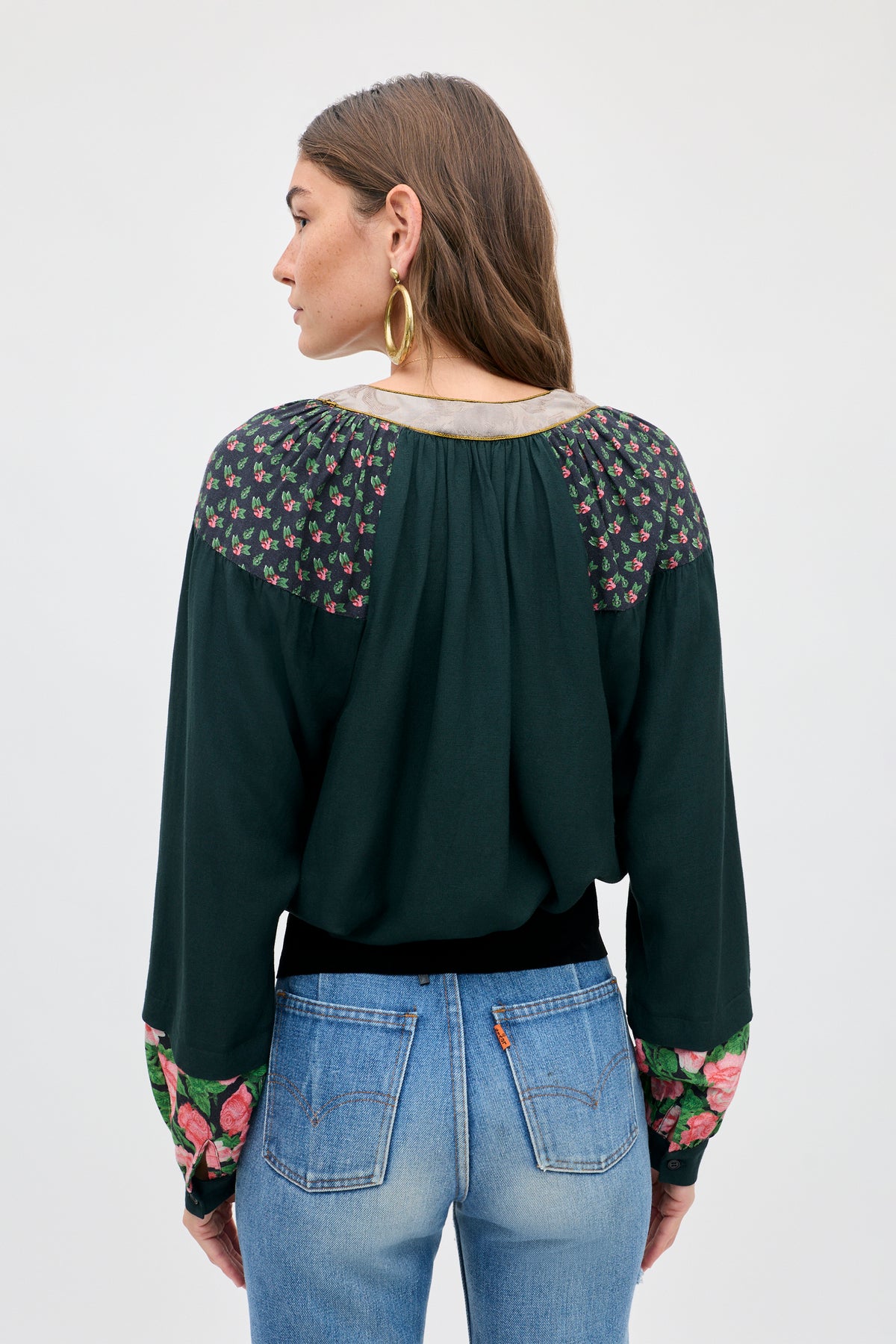A person seen from behind wearing the Bria - Rose Mix Pink dark green long-sleeved blouse with floral patterns on the shoulders and cuffs, paired with blue jeans.