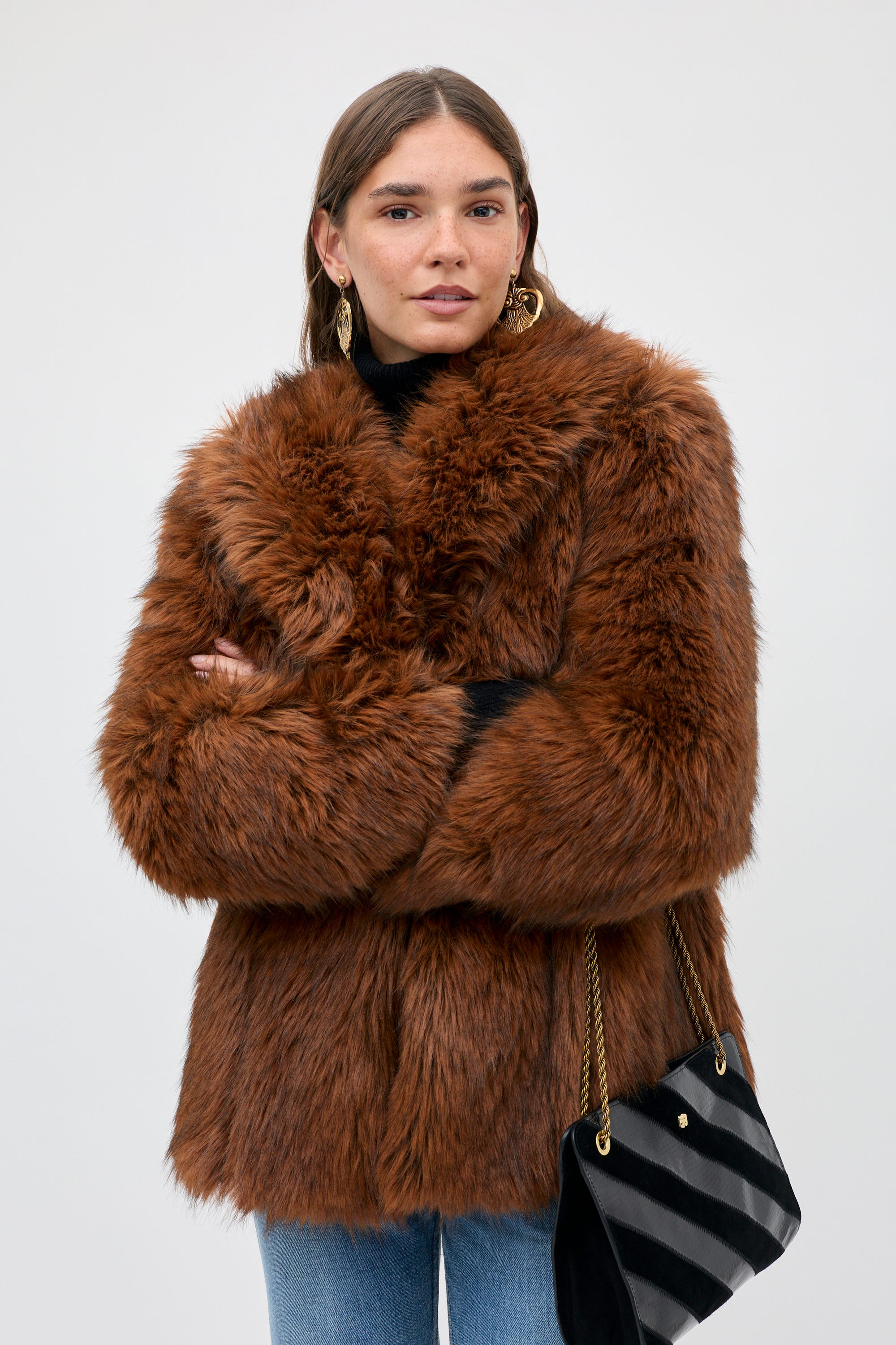 A person wearing a Cybil - Brown faux fur coat over a black turtleneck and jeans, with a shoulder bag.