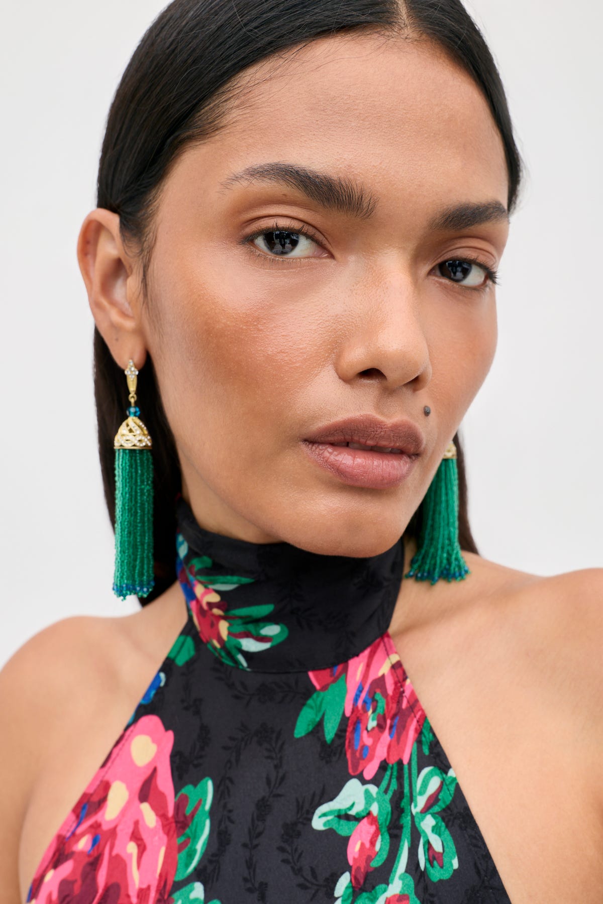 Close-up of a woman wearing Alea - Green tasseled earrings with gold filigree caps and a black floral halter top.